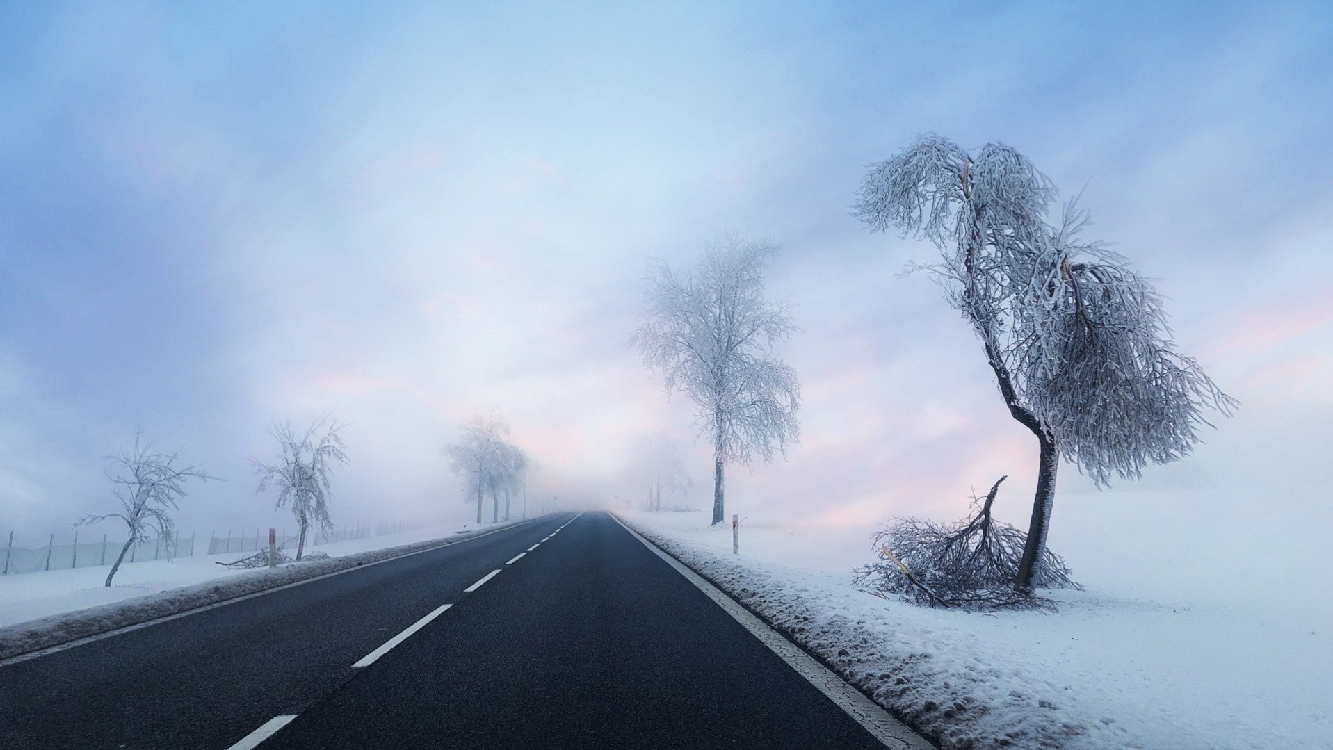 A snow-covered road disappears into thick morning fog
