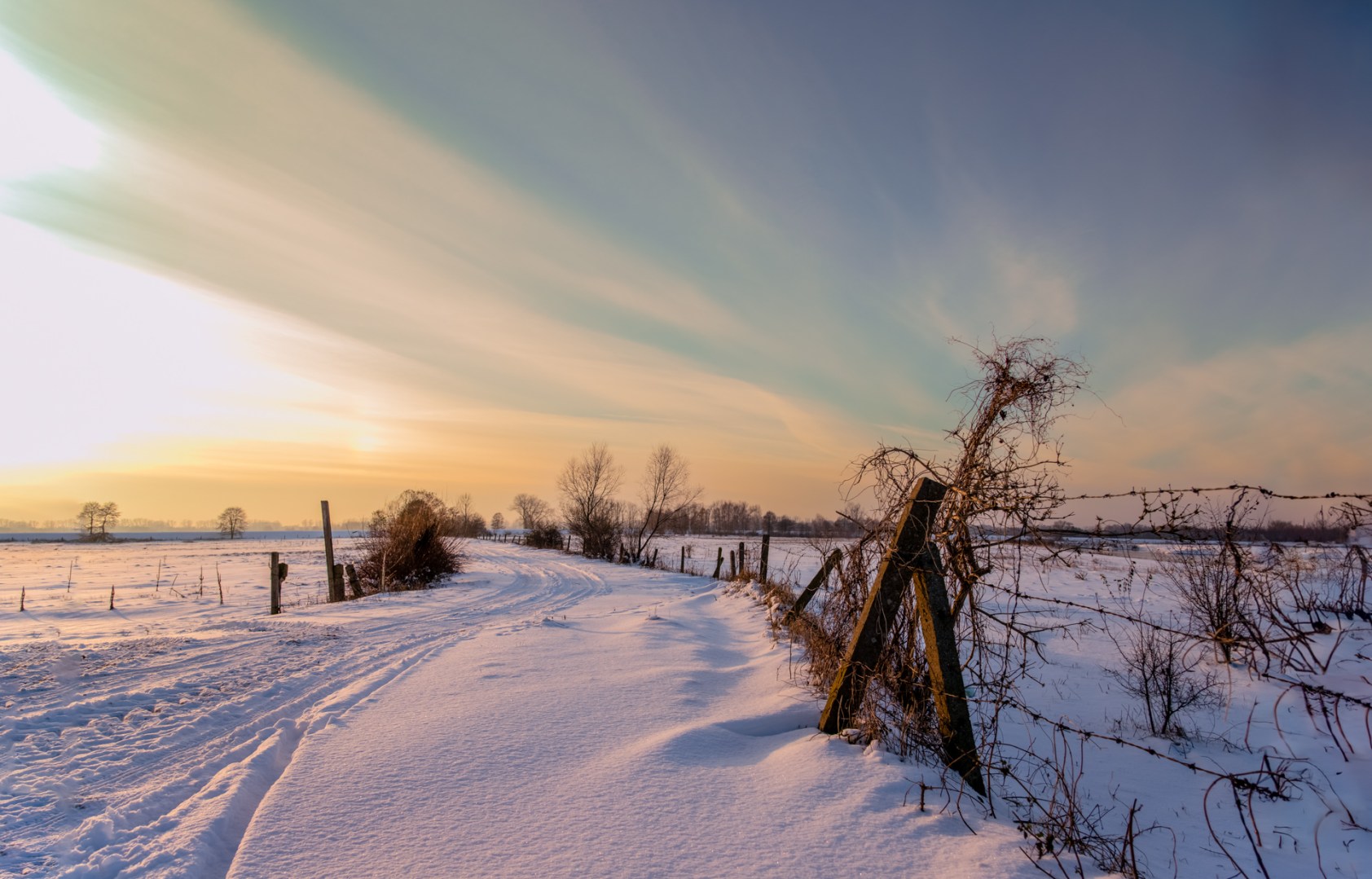 Snowy field with wooden fence under dramatic twilight sky