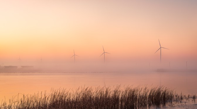 Wind turbines rise from morning mist in a glowing pink sunrise