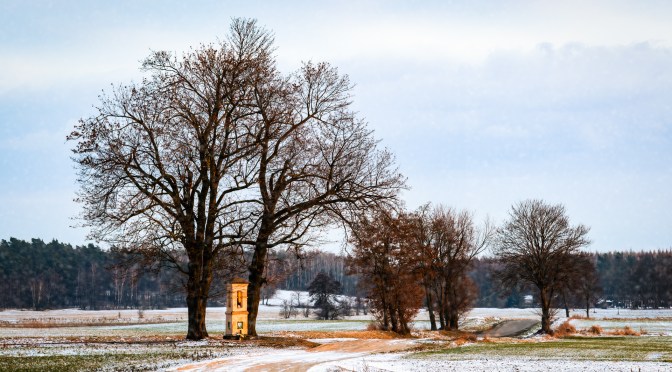 Small chapel between bare winter trees in a snow-covered countryside