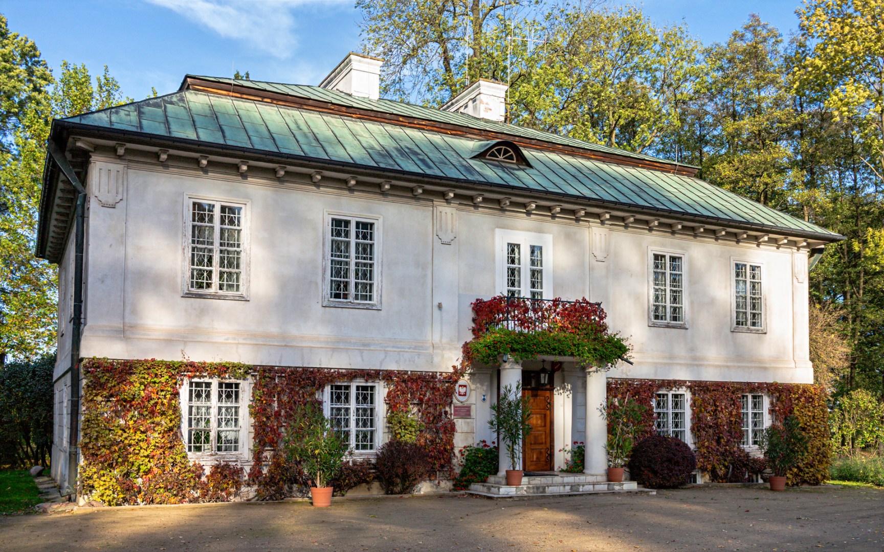 Side view of heritage manor house in Poland with green roof and climbing vines in a park setting