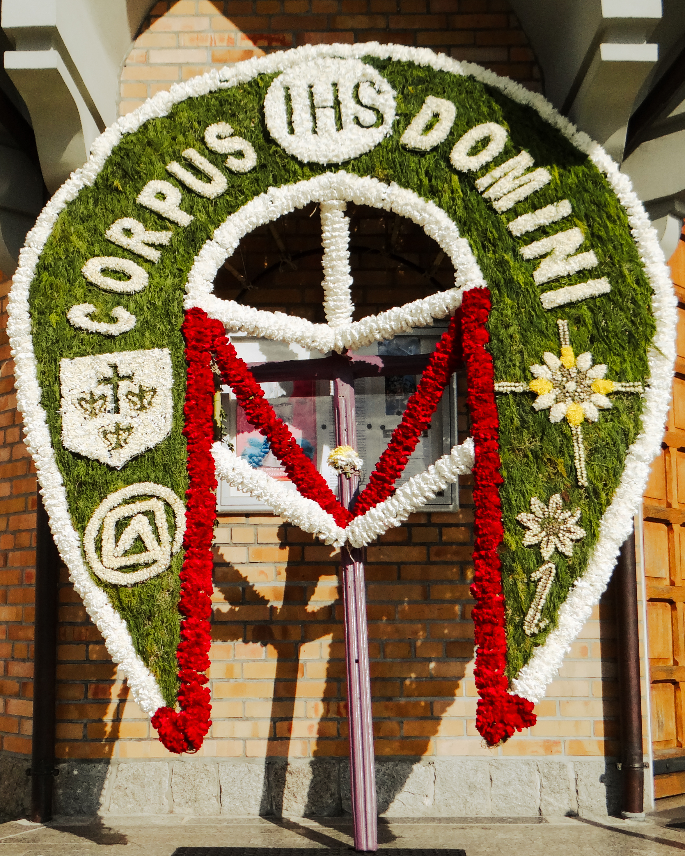 Floral banner reading Corpus Domini at a church entrance in Spycimierz