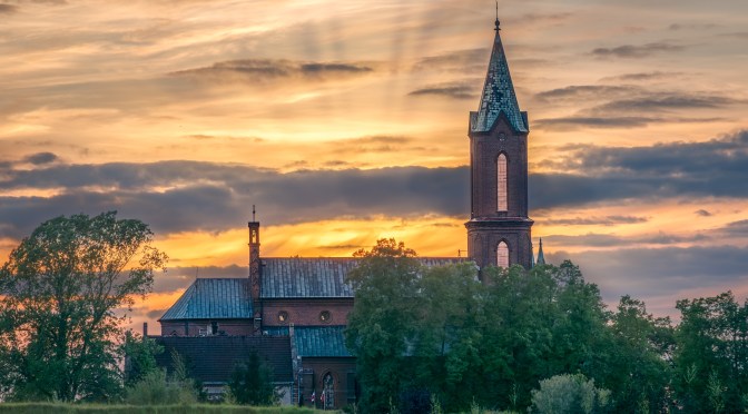 Sunset over the Church of the Immaculate Conception in Wojkow, Poland, with a blooming rapeseed field in the foreground and dramatic sky in the background