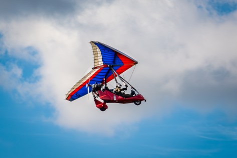 Red and blue ultralight hang glider flying in sunny sky