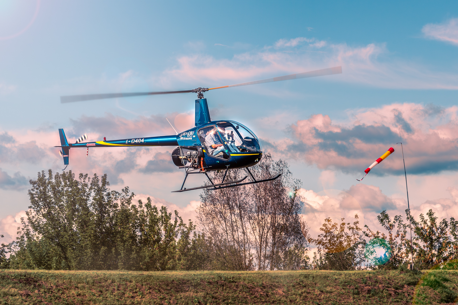 Blue helicopter hovering near landing pad at sunset