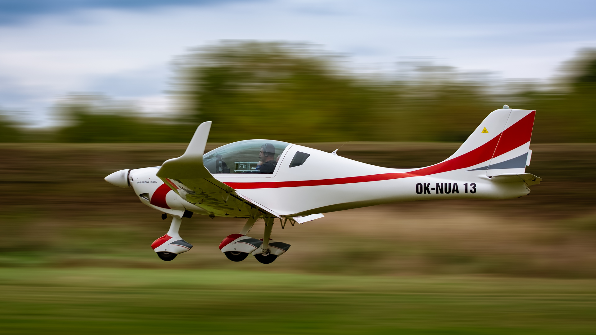 White and red single-engine plane flying low over grass at high speed