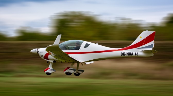 White and red single-engine plane flying low over grass at high speed