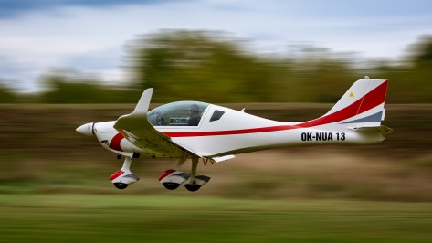 White and red single-engine plane flying low over grass at high speed
