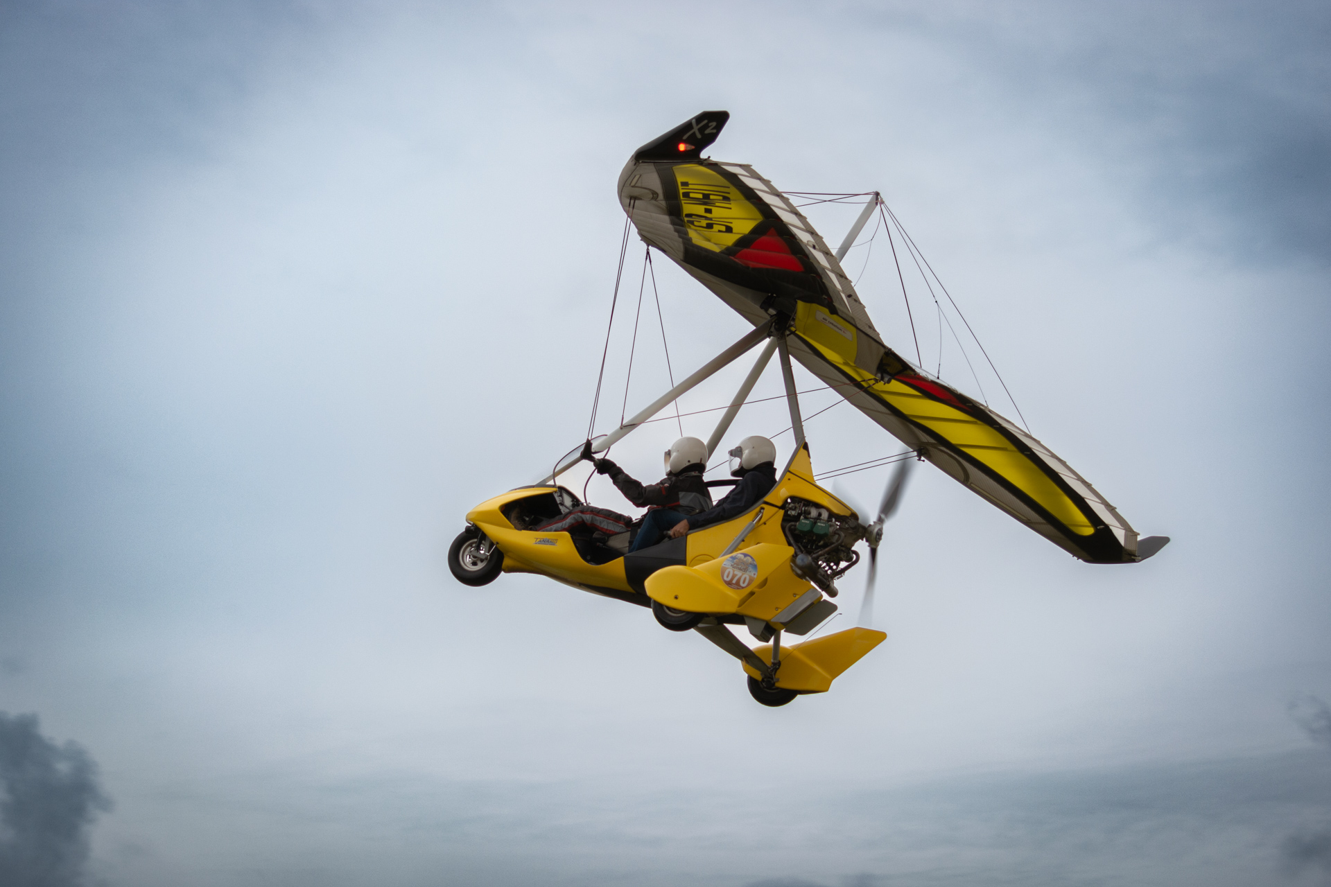 Yellow ultralight trike flying in cloudy weather during air show