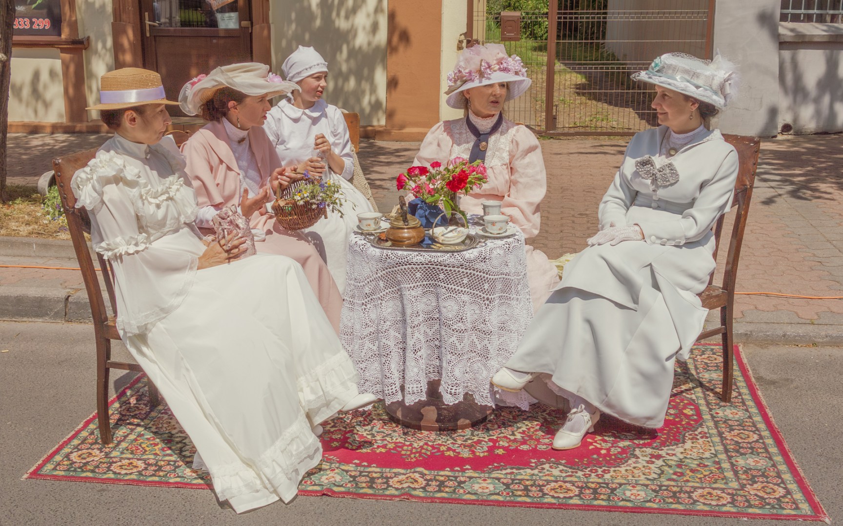 Women in white Edwardian-style dresses and hats sitting at a tea table during a historical reenactment in Poland