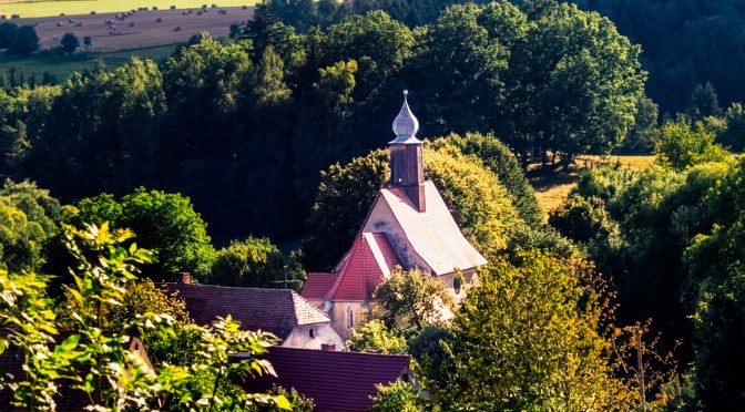 Countryside church with red roof among fields, meadows, and forest ridges on a sunny summer day