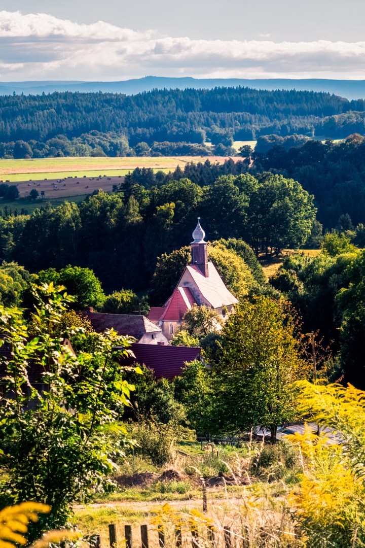 Countryside church with red roof among fields, meadows, and forest ridges on a sunny summer day