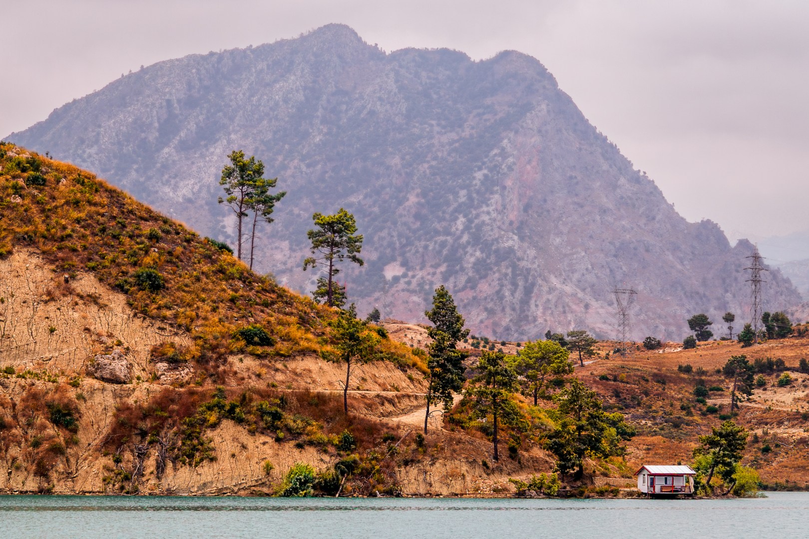 A small hut by a turquoise lake in Turkey, framed by orange hills and a towering mountain