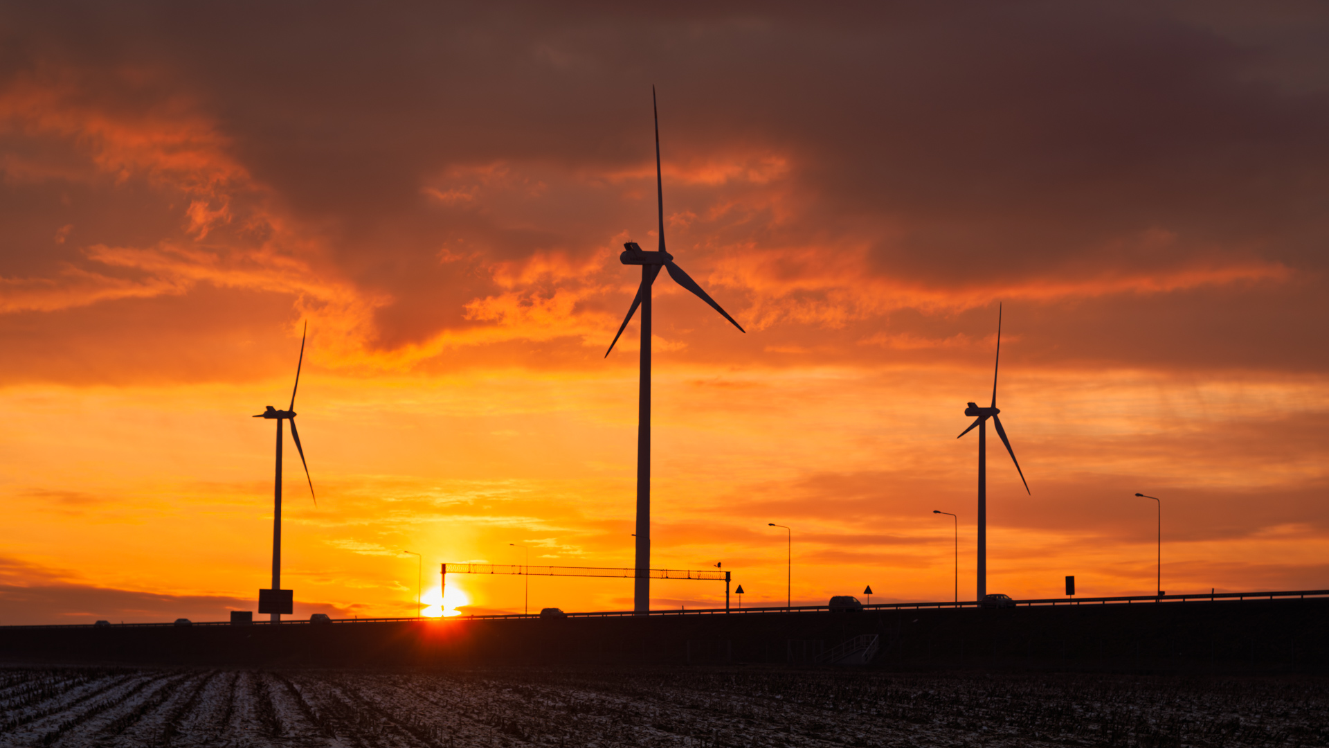 Wind turbines at sunset with warm orange and magenta sky over a snowy winter field in December