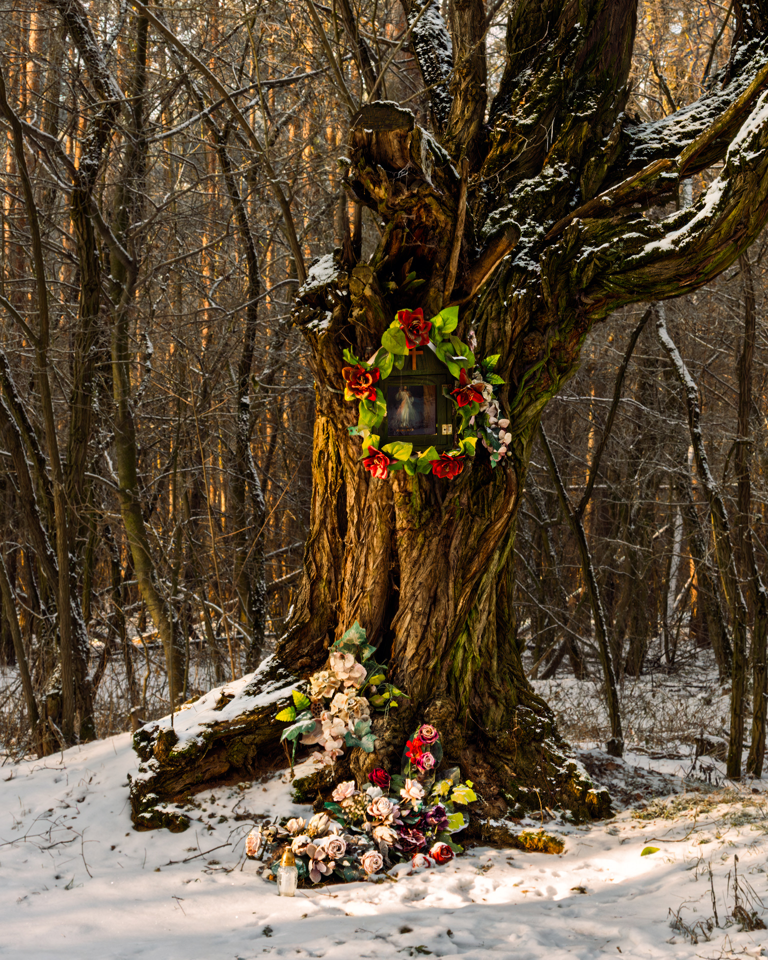 Roadside shrine in Poland during winter, decorated with flowers and candles, set in a quiet forest landscape