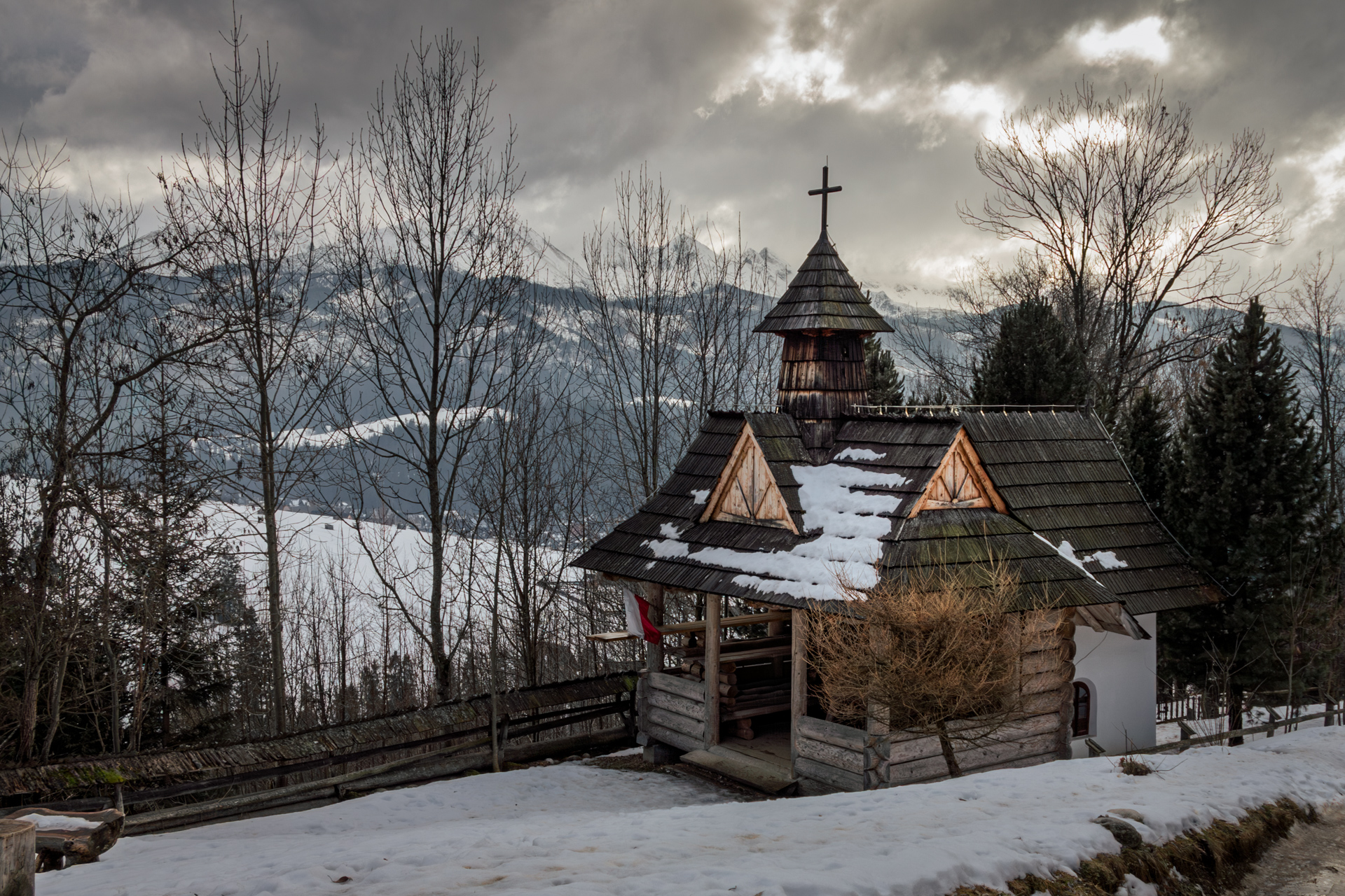 Winter scene of the Kaplica na Tarasówce chapel in the Tatra Mountains, snow-covered and serene, surrounded by mountain views