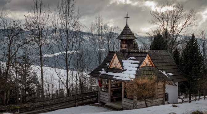 Winter scene of the Kaplica na Tarasówce chapel in the Tatra Mountains, snow-covered and serene, surrounded by mountain views